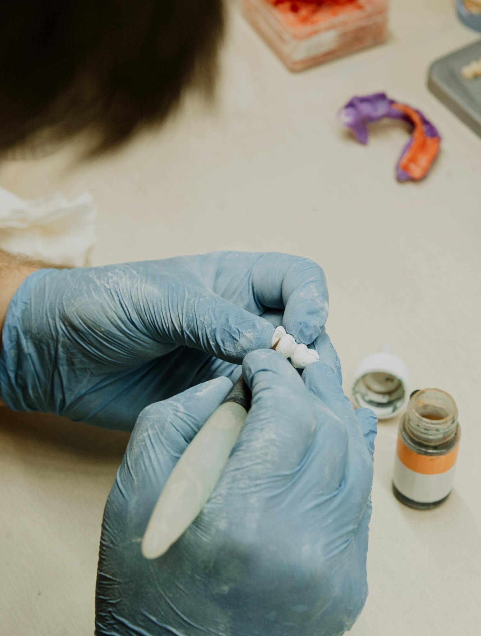 Crop anonymous orthodontist in latex gloves creating fake teeth using dental tools while sitting at table in dental clinic